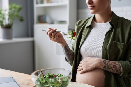 Téléchargez les photos : Gros plan de la jeune femme enceinte manger de la salade pour le petit déjeuner et regarder la vidéo, copier l'espace - en image libre de droit