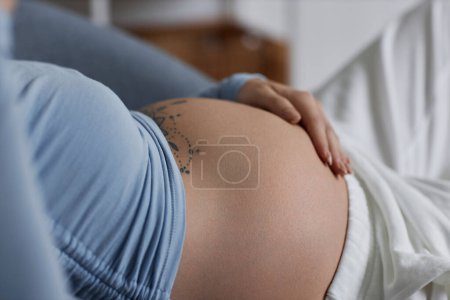 Photo for Side view of young woman with tattooed pregnant belly wearing blue, minimal - Royalty Free Image