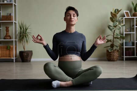 Foto de Mujer joven embarazada disfrutando de una sesión de yoga prenatal y sentada en posición de loto con los ojos cerrados - Imagen libre de derechos