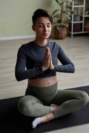 Foto de Retrato vertical de una joven embarazada meditando mientras disfruta de una sesión de yoga prenatal y se sienta en posición de loto en el suelo - Imagen libre de derechos