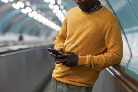 Téléchargez les photos : Gros plan d'un homme d'affaires afro-américain tapant un message sur un smartphone debout sur un escalator dans le métro - en image libre de droit