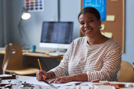 Téléchargez les photos : Portrait de l'architecte afro-américain souriant à la caméra tout en dessinant un plan à la table - en image libre de droit
