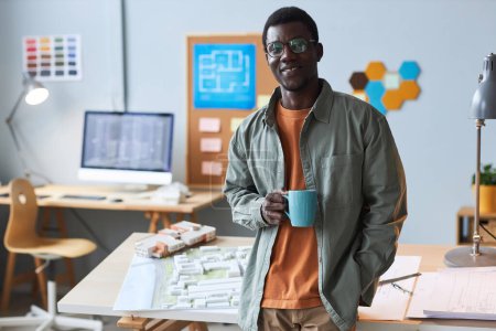 Téléchargez les photos : Portrait de l'architecte afro-américain buvant du café debout au bureau et souriant à la caméra - en image libre de droit