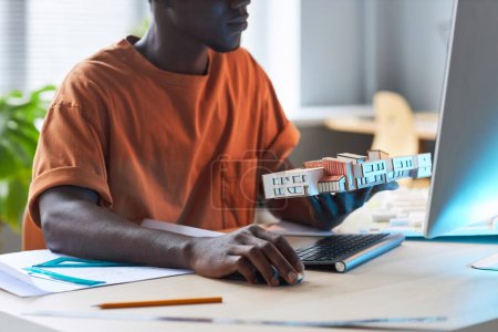 Téléchargez les photos : Jeune ingénieur afro-américain utilisant l'ordinateur pour développer un nouveau projet de construction sur son lieu de travail - en image libre de droit