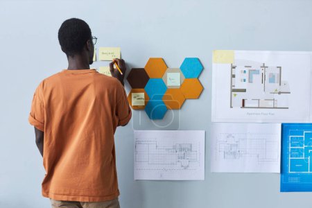 Téléchargez les photos : Vue arrière de l'architecte afro-américain prenant des notes sur le projet de construction de nouveaux murs - en image libre de droit