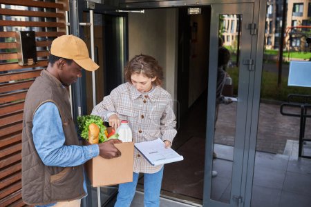 Téléchargez les photos : Portrait de jeune femme acceptant la livraison de nourriture à l'extérieur et examinant les produits d'épicerie frais, l'espace de copie - en image libre de droit