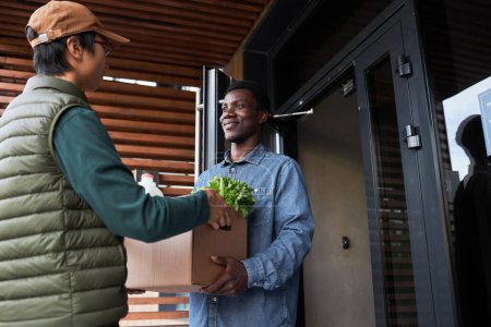 Téléchargez les photos : Portrait taille haute de jeune homme noir acceptant la livraison d'épicerie à l'extérieur et souriant - en image libre de droit