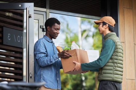 Photo for Side view portrait of black young man accepting grocery delivery outdoors and smiling - Royalty Free Image