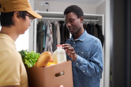 Téléchargez les photos : Portrait taille haute de jeune homme noir inspectant la livraison d'épicerie fraîche à la maison - en image libre de droit