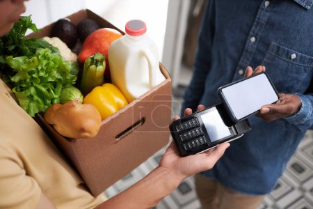 Foto de Primer plano del hombre irreconocible que paga por la entrega de comestibles a través de teléfono inteligente NFC - Imagen libre de derechos