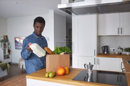Photo for Waist up portrait of black man unpacking fresh groceries in kitchen interior, copy space - Royalty Free Image