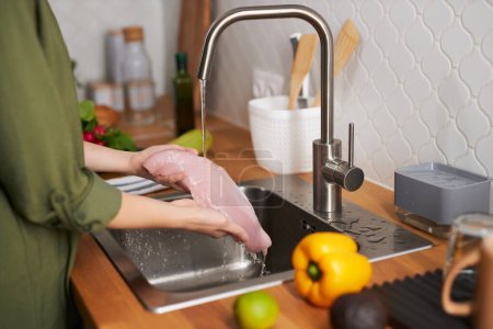 Photo for Closeup of young woman washing chicken breast meat in tap water, copy space - Royalty Free Image