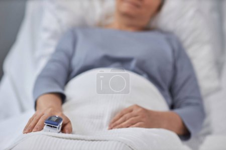 Téléchargez les photos : Gros plan de la patiente âgée allongée sur son lit et examinant sa tension artérielle avec un dispositif spécial sur son doigt - en image libre de droit