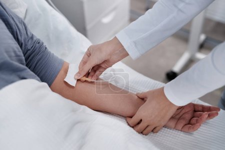 Foto de Primer plano del médico colocando un goteo intravenoso al paciente por vía intravenosa mientras ella yacía en la cama en la sala de hospital - Imagen libre de derechos