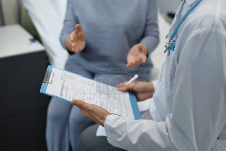 Téléchargez les photos : Gros plan du médecin examinant la carte médicale du patient et lui parlant pendant sa visite en salle - en image libre de droit