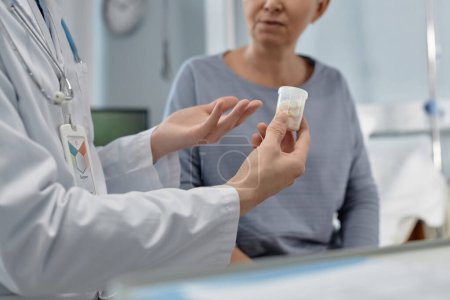 Téléchargez les photos : Gros plan du médecin tenant une bouteille avec des pilules les prescrivant au patient pour le traitement pendant qu'il est assis dans la salle d'hôpital - en image libre de droit