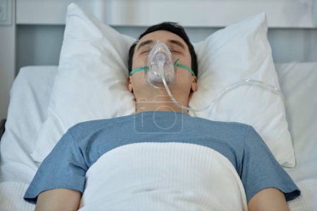 Photo for Young man in oxygen mask on his face lying on bed during rehabilitation in hospital - Royalty Free Image