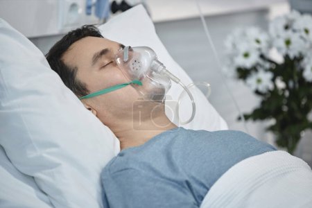 Téléchargez les photos : Jeune patient avec masque à oxygène couché à l'hôpital pendant sa rééducation - en image libre de droit