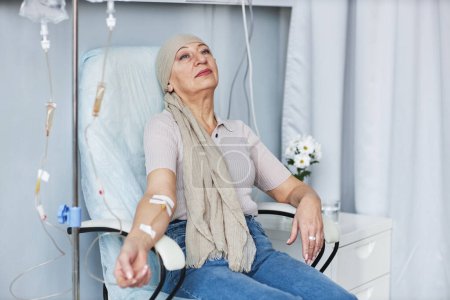 Foto de Retrato de una mujer mayor cansada sentada en silla con goteo intravenoso durante el tratamiento de quimioterapia - Imagen libre de derechos