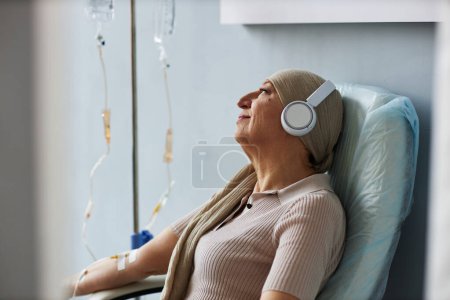 Foto de Retrato de vista lateral de una mujer mayor escuchando música durante el tratamiento de quimioterapia, espacio para copiar - Imagen libre de derechos