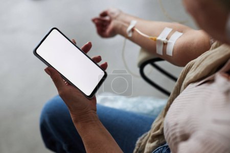 Foto de Primer plano de la mujer mayor sosteniendo teléfono inteligente con pantalla en blanco durante el tratamiento por goteo IV, espacio de copia - Imagen libre de derechos