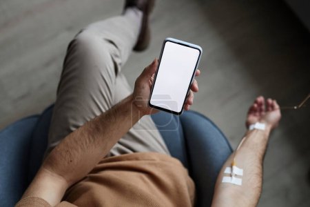 Foto de Vista superior del hombre usando el teléfono inteligente con la maqueta de pantalla blanca durante el tratamiento por goteo IV, espacio de copia - Imagen libre de derechos