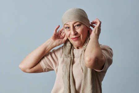 Foto de Retrato de cintura hacia arriba de una mujer calva madura con pañuelo en la cabeza mirando a la cámara y sonriendo con confianza - Imagen libre de derechos