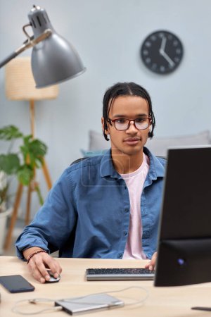 Téléchargez les photos : Portrait vertical de jeune homme noir utilisant un ordinateur à la maison tout en étudiant ou en écrivant du code - en image libre de droit