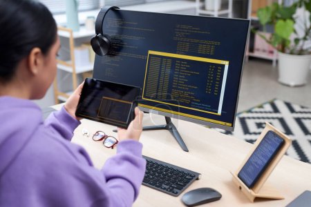 Téléchargez les photos : Vue latérale du programmeur informatique féminin tenant la tablette et le code d'écriture pour les appareils mobiles sur le lieu de travail - en image libre de droit