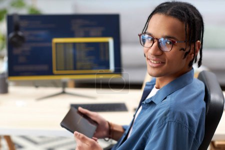 Téléchargez les photos : Portrait de programmeur d'ordinateur souriant tenant la tablette et regardant la caméra sur le lieu de travail - en image libre de droit