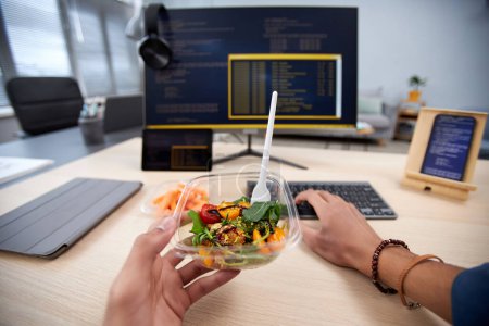 Photo for POV of unrecognizable man eating takeout lunch at workplace while programming code, copy space - Royalty Free Image