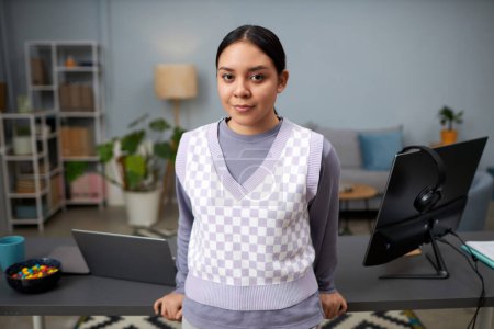 Foto de Retrato de cintura hacia arriba de una joven latinoamericana mirando a la cámara mientras está de pie en el lugar de trabajo de su oficina - Imagen libre de derechos