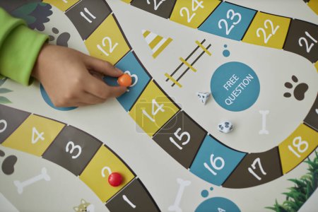 Top view closeup of child playing board game with small hand moving game piece, copy space