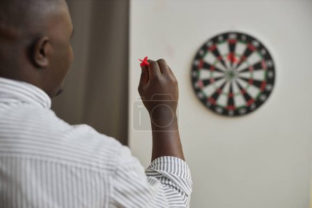 Minimal back view of African American man playing darts and aiming shot, copy space