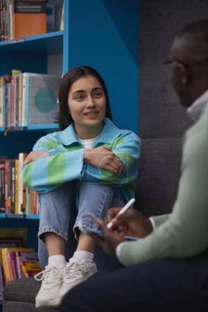 Foto de Retrato vertical de una adolescente estresada hablando con un terapeuta de salud mental en la biblioteca de la universidad - Imagen libre de derechos