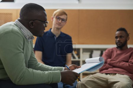 Photo for Side view portrait of black man as male psychologist consulting young people in support group - Royalty Free Image