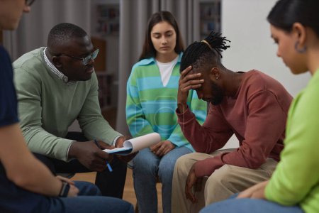 Téléchargez les photos : Portrait latéral d'un homme noir en difficulté pleurant dans un cercle de soutien et partageant son histoire avec un thérapeute - en image libre de droit