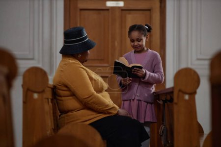 Téléchargez les photos : Petite fille afro-américaine lisant la prière de la Bible à sa grand-mère lors de leur visite à l'église - en image libre de droit