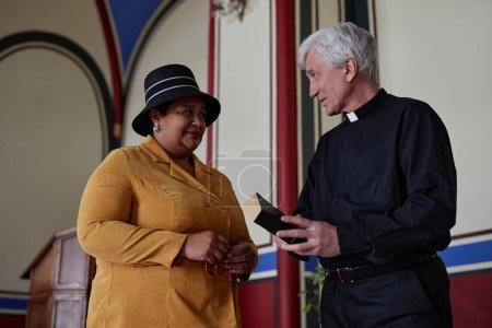Foto de Mujer creyente afroamericana hablando con sacerdote mientras están de pie en la iglesia - Imagen libre de derechos