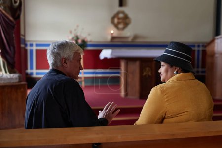 Téléchargez les photos : Vue arrière du prêtre principal discutant de la cérémonie avec une femme assise sur un banc lors de sa visite à l'église - en image libre de droit