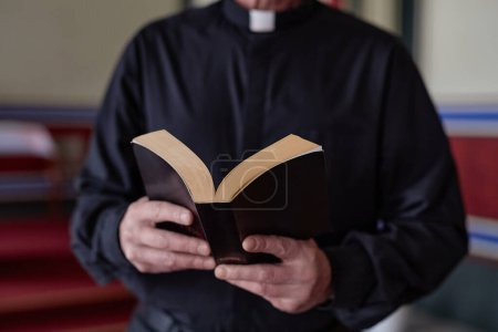Photo for Close-up of priest reading Bible book during ceremony standing near the altar in church - Royalty Free Image