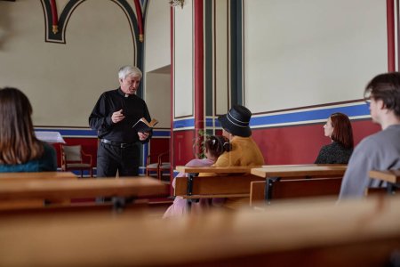 Téléchargez les photos : Grand prêtre tenant livre et sermon de lecture pour les croyants qui sont assis et l'écoutent à l'église - en image libre de droit