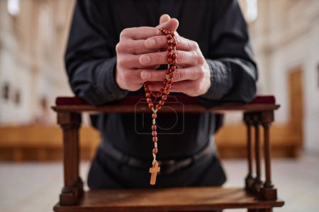 Photo for Close-up of senior man with rosary beads praying standing behind the altar in church - Royalty Free Image