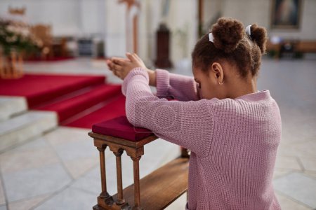 Photo for African American little girl standing behind the altar and praying in church - Royalty Free Image