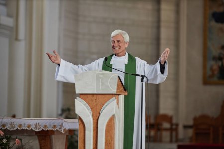 Photo for Smiling senior priest in formalwear greeting people in church while standing behind the altar - Royalty Free Image