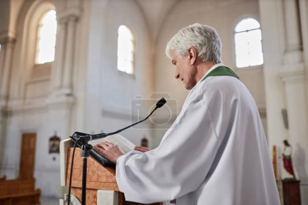 Foto de Sacerdote principal leyendo sermón en micrófono parado detrás del altar en la ceremonia en la iglesia - Imagen libre de derechos