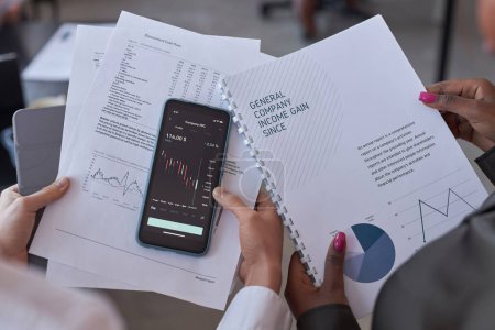 Photo for High angle view of colleagues holding documents and smartphone with graphs, they working with financial documents - Royalty Free Image
