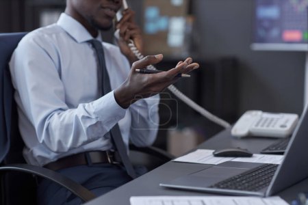 Close-up of African American broker talking on the phone with customer while sitting at his workplace with laptop