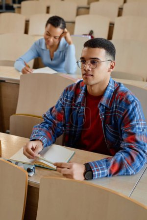 Photo for Schoolboy in eyeglasses sitting at desk with books during lecture in lecture hall - Royalty Free Image