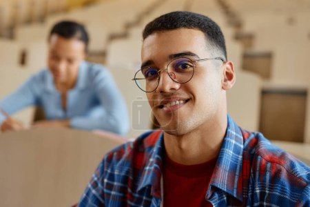 Foto de Retrato de colegial con anteojos sonriendo a la cámara mientras estaba sentado en la conferencia con sus compañeros de clase - Imagen libre de derechos